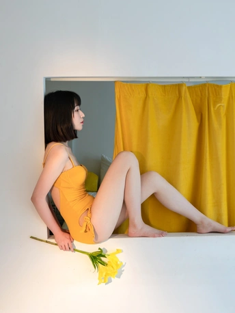 一个穿着橙色连衣裙的年轻女子盘腿坐着 手里拿着一朵黄色的花