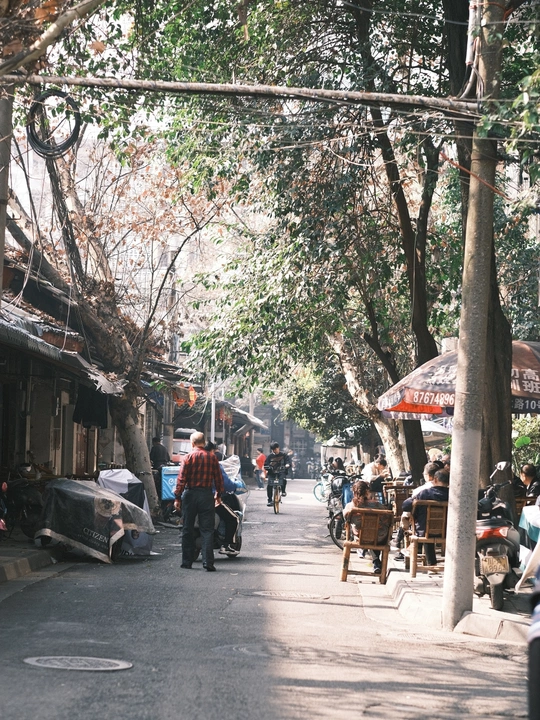 人们走在停有汽车和摩托车的小巷