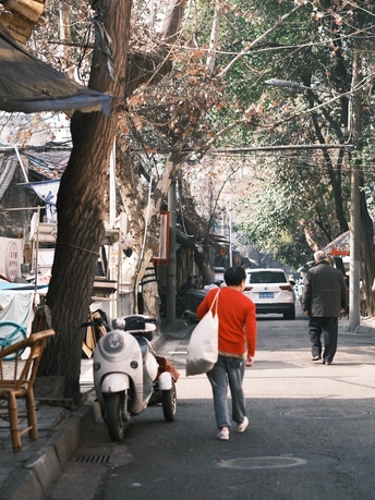 一条街道上停着一辆滑板车 树下有人走人行道。