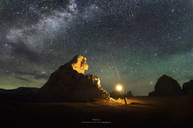 在沙漠中一个夜晚星空下的山顶站立着一个男子