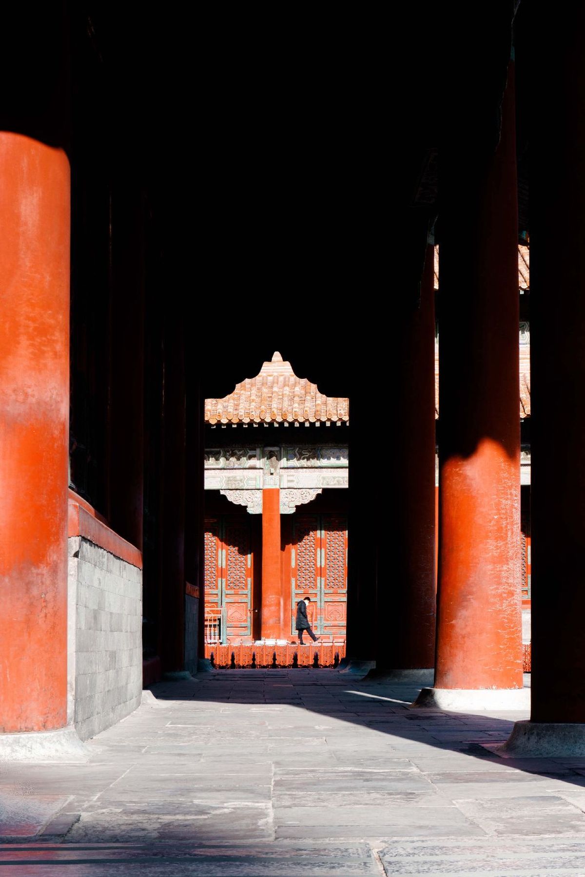 一个人走过一座庙宇 庙宇内有大红色的墙壁和柱子。