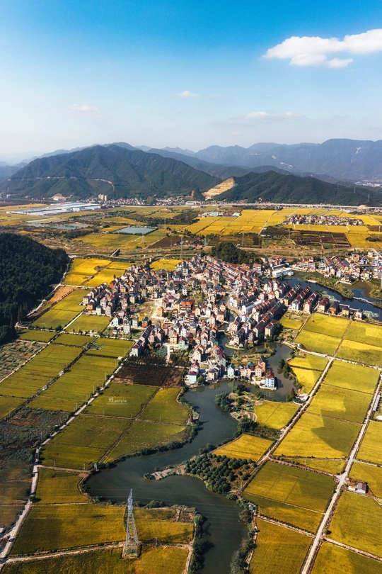 一个小村庄或小镇的 aerial view 周围有河流和远处的山脉。