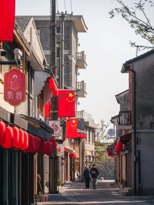 一条狭窄的老镇街道 人们沿着街道走 建筑物上挂着红旗。