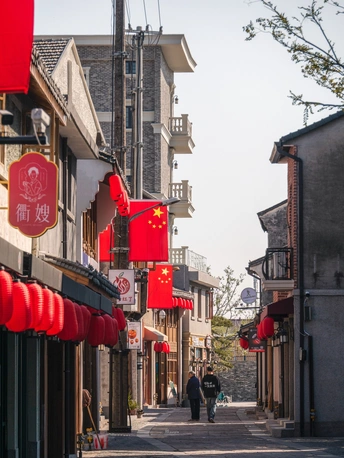 一条狭窄的老镇街道 人们沿着街道走 建筑物上挂着红旗。