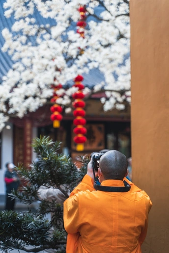 一位穿着橙色夹克的女人走在街上 同时还在通话中 背景中有一栋建筑和一棵树。