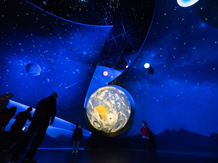 人们在博物馆里站着 注视着一个带有月亮的大球体。
