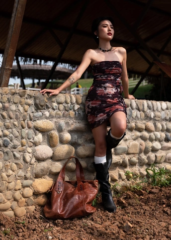 一位穿着连衣裙和靴子 倚靠在墙上 带着钱包和手提包的年轻女子