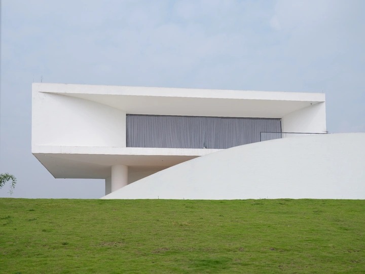 一座白色的现代房子坐落在山坡上 周围是绿色的草地。