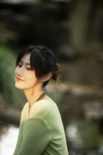 一个穿着绿色毛衣的年轻女子站在小溪边
