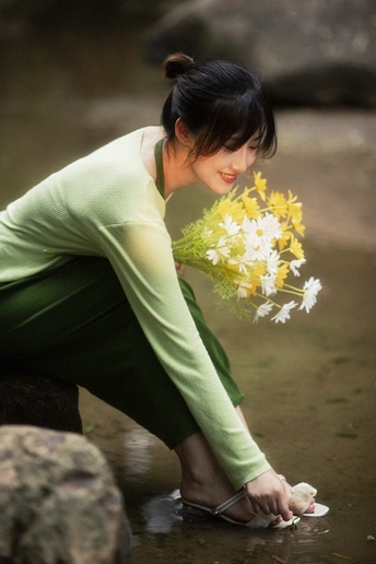 一个年轻女子跪在河边的岩石上 手里拿着一束花