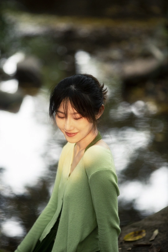 一位身穿绿色衣服的年轻女子站在小溪边的岩石上