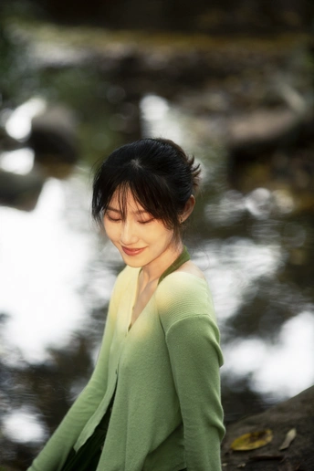 一位身穿绿色衣服的年轻女子站在小溪边的岩石上
