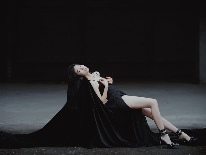 一个穿着黑色连衣裙的美女躺在黑暗的房间里地板上