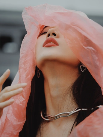 一位女士身穿粉色雨衣 用雨伞遮住脸。