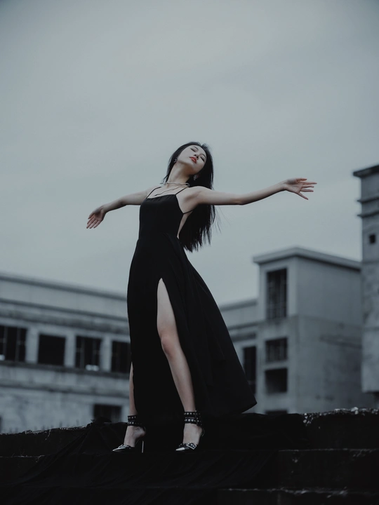 一个穿黑色连衣裙的女人站在一栋建筑的屋顶上 带着一把伞。