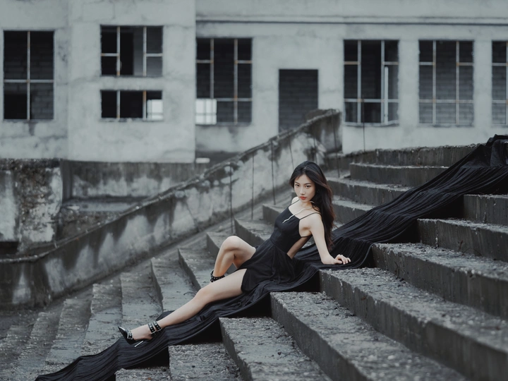 美丽的年轻女子穿着黑色连衣裙坐在台阶上 带着雨伞。