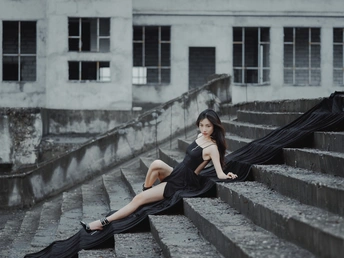 美丽的年轻女子穿着黑色连衣裙坐在台阶上 带着雨伞。