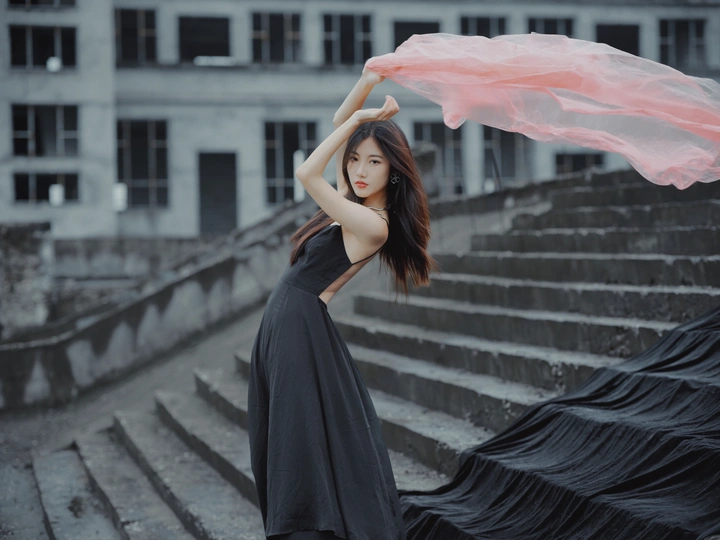 美丽的年轻女子穿着黑色连衣裙 戴着红色围巾站在楼梯上 拿着粉色雨伞。