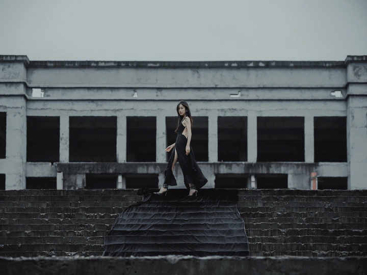 一个穿黑色连衣裙的女人带着一把伞走下一些台阶 伞站在一栋建筑的屋顶上。