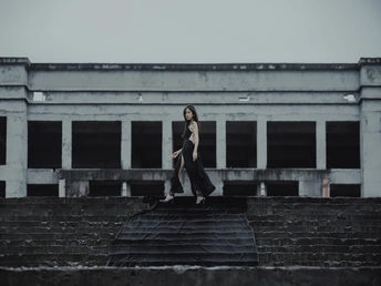 一个穿黑色连衣裙的女人带着一把伞走下一些台阶 伞站在一栋建筑的屋顶上。