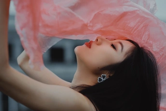 一个穿着粉红色连衣裙的年轻女子举着一把塑料伞在头上