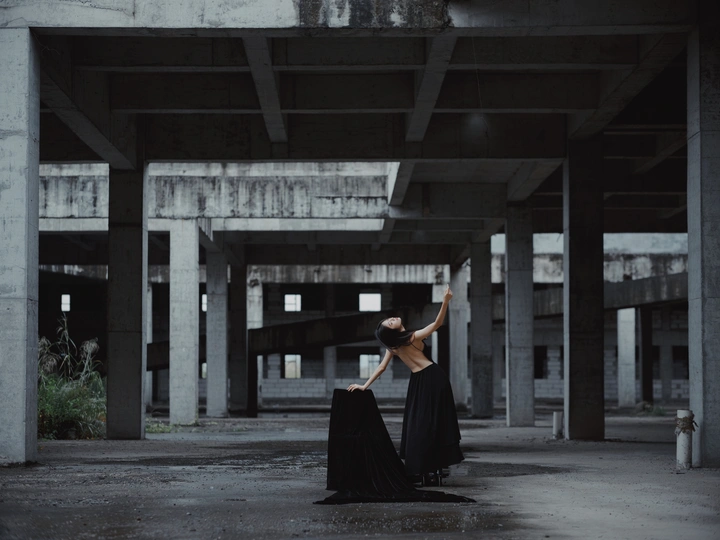 一个穿着黑色连衣裙的女人站在一个空荡荡的建筑中 手里拿着一把伞。