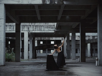 一个穿着黑色连衣裙的女人站在一个空荡荡的建筑中 手里拿着一把伞。