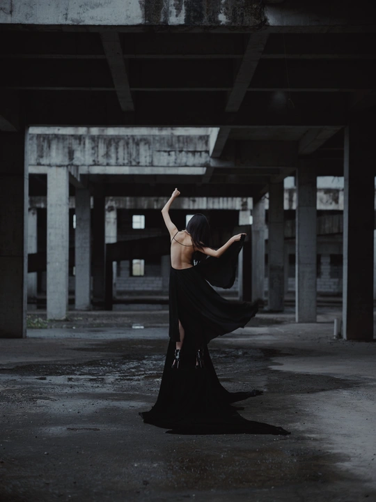 一个穿着黑色长裙的女人站在一座废弃的建筑中 手里拿着一把雨伞。