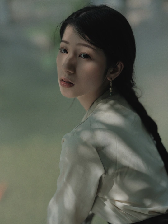 一位年轻女子穿着一件白色衬衫站在窗户旁边