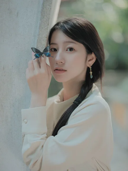 一位穿着全白的年轻女子站在一个有蝴蝶图案的墙上。