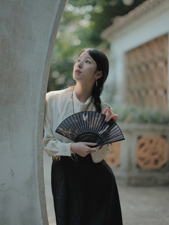 一位穿着传统服装的年轻女子拿着黑色扇子