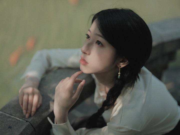 一位年轻女子坐在墙上 手伸向水面。