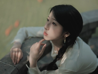 一位年轻女子坐在墙上 手伸向水面。