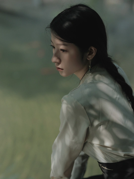 一位穿着白色衬衫的年轻女子站在水边