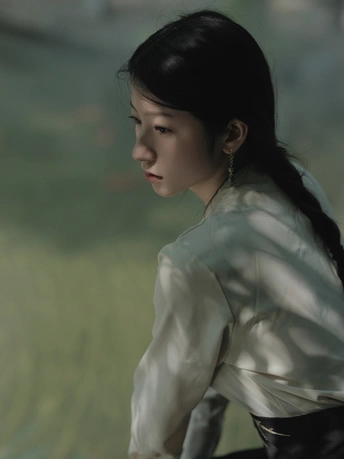 一位穿着白色衬衫的年轻女子站在水边