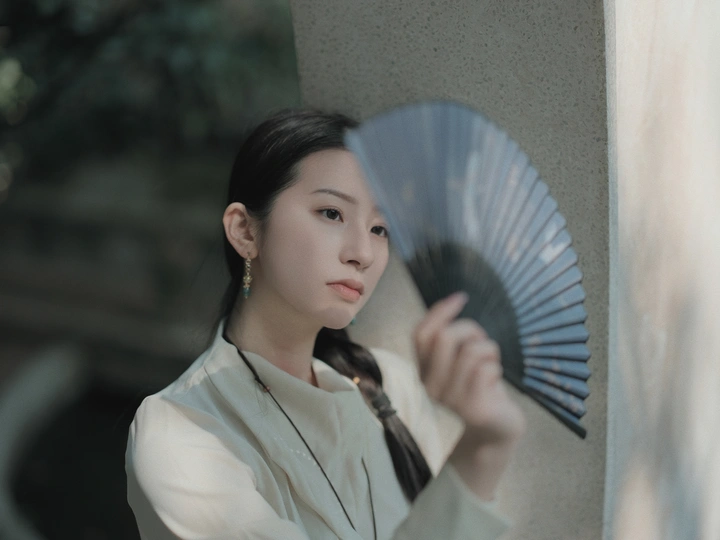 一位年轻女子穿着一件白色领带 手里拿着一把扇子。