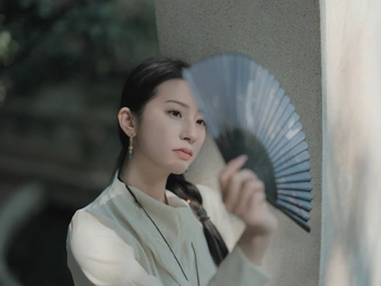 一位年轻女子穿着一件白色领带 手里拿着一把扇子。