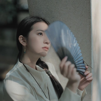 一位年轻女子穿着一件蓝色雨伞站在一根柱子旁边 手里拿着一把扇子。