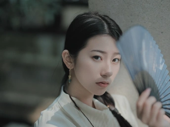 一位年轻女子穿着一件白色雨伞 手里拿着一把蓝色扇子。