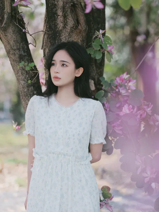 一位穿着白色连衣裙的年轻女子站在一棵树下