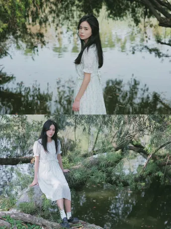 一个穿着白色连衣裙的年轻女子站在一条流水中的倒下的大树旁