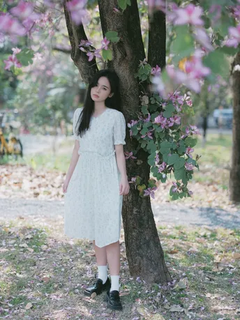 站在开满花的树下的穿着白裙子的年轻女子