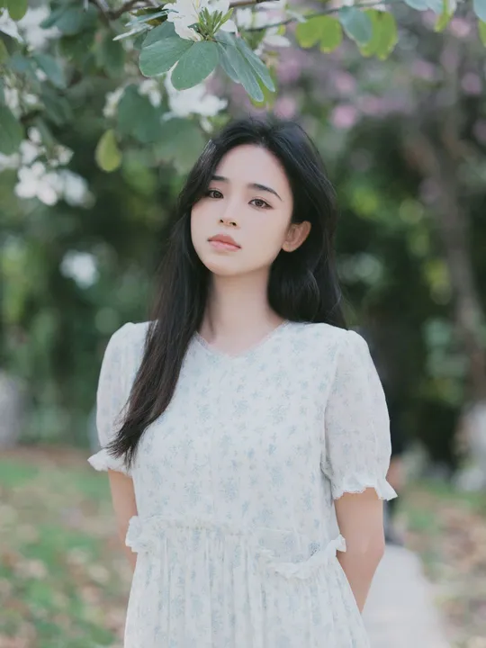 一位穿着白色连衣裙的年轻女子站在一棵树下