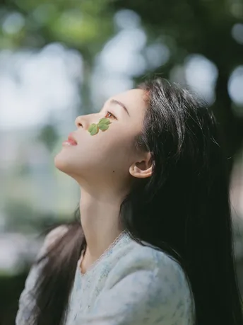 一位年轻女子仰望着天空 眼中带着一片树叶。