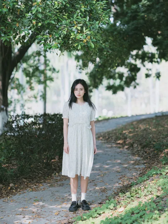 一位穿着白色连衣裙的年轻女子站在公园的小径上