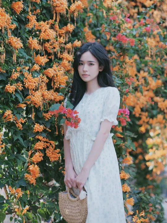 一位穿着白色连衣裙站在橙花前的女性