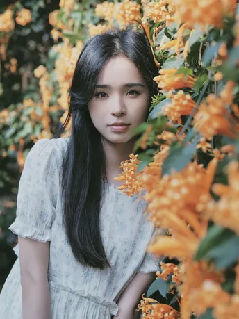 一位穿着白色连衣裙的年轻女子在黄色花朵前摆姿势照相