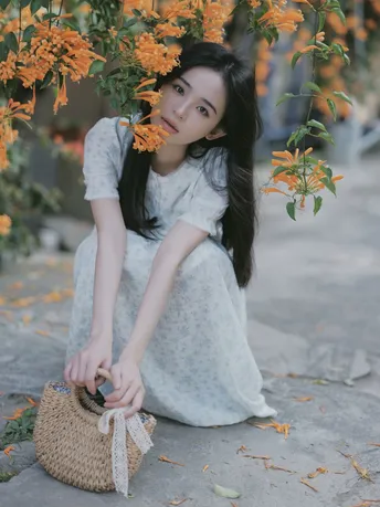 一位穿着白色连衣裙的年轻女子抱着一个包 坐在有橙色花朵的树下