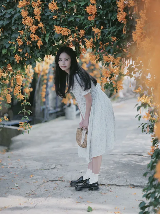 一位穿着白色连衣裙的年轻女子站在一棵树下