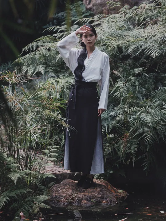 一位穿着白色衣服的女子站在一条溪流中的岩石上